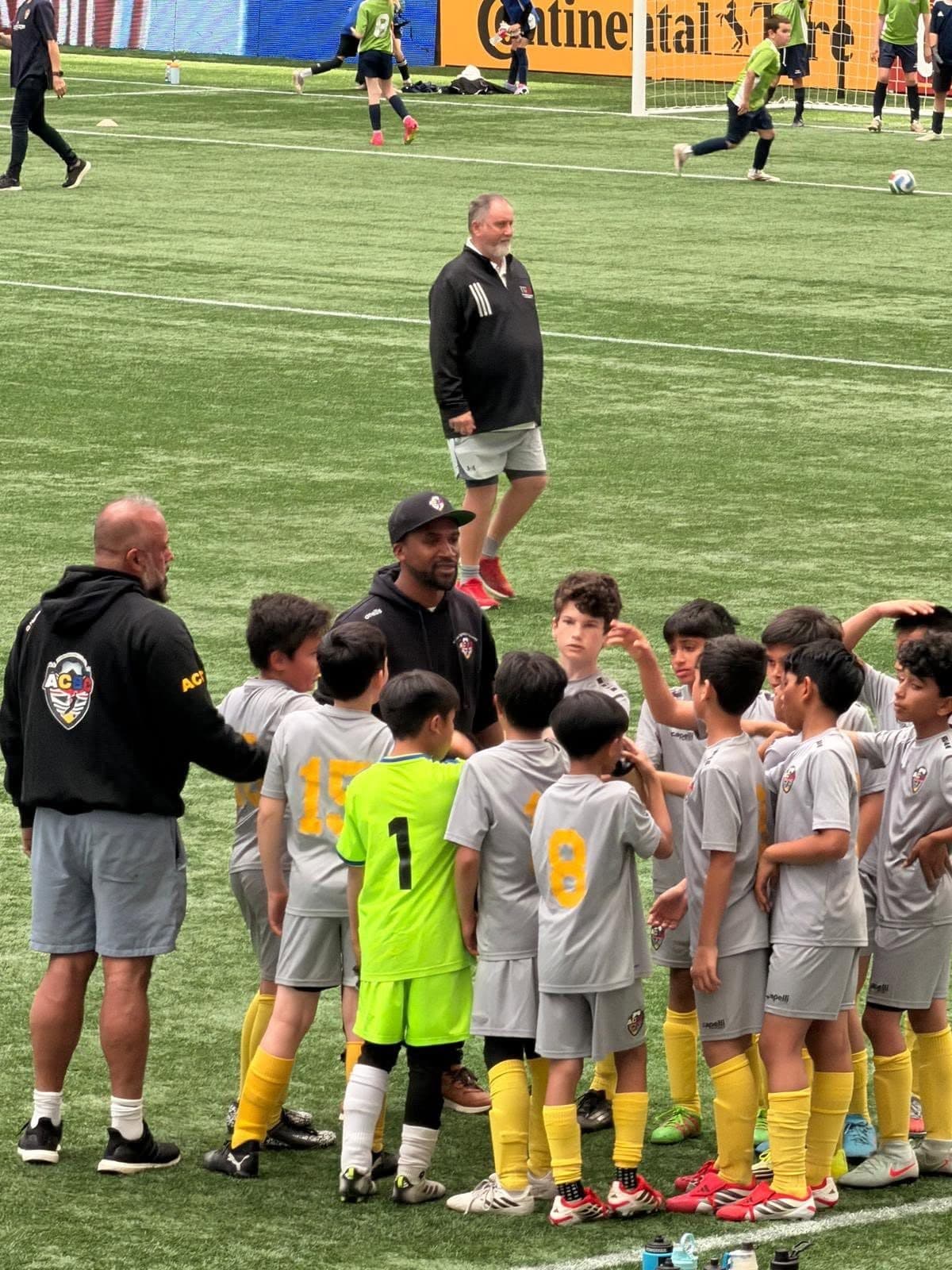 An ACBC coach talking to the squad in a huddle on the pitch before kick-off