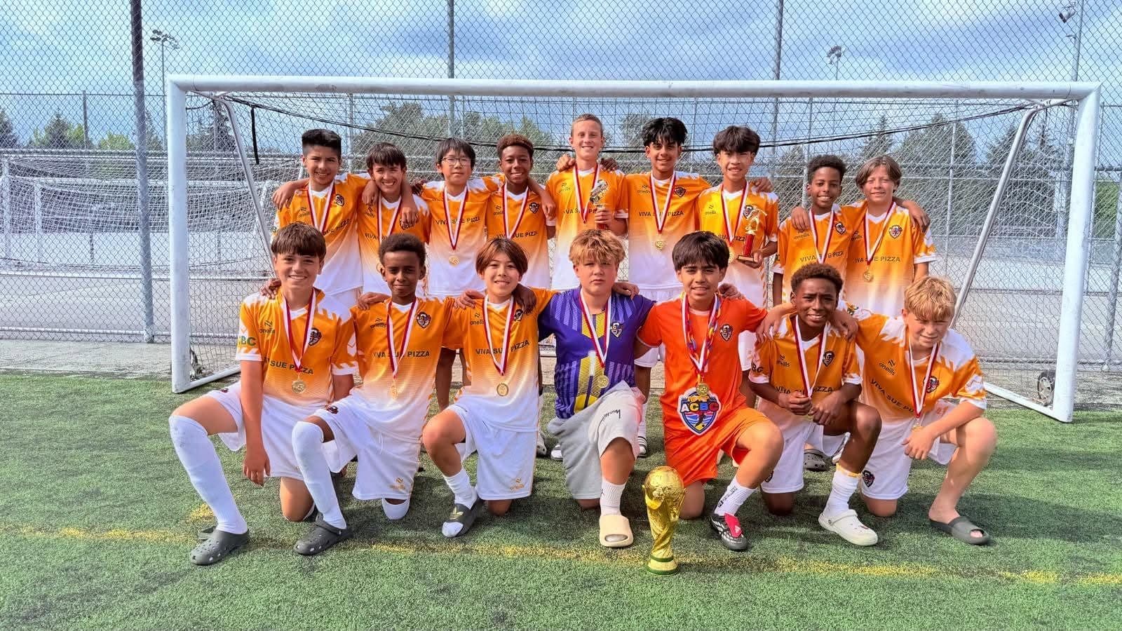 An ACBC squad wearing medals around a trophy in front of the goal